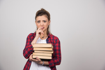 An upset woman holding a stack of books on a gray wall