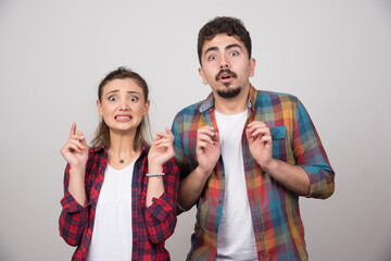 A young couple over gray background with fingers crossing and wishing the best