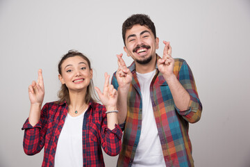 A young couple over gray background with fingers crossing and wishing the best