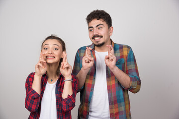 Naklejka premium A young couple over gray background with fingers crossing and wishing the best