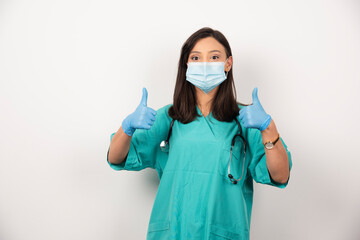 Female doctor in mask showing thumbs up on white background