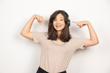 Young woman pointing on headphones on white background