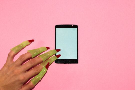 mobile phone with pastel blue screen on pink background and hand with witch green fingers searching, phone as copy space, creative concept, modern design