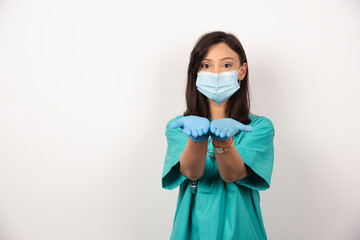Young doctor in medical mask and gloves opening her hands on white background