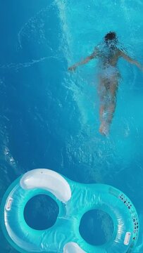 Pretty woman jumps from a mattress in a swimming pool - view from above - Vertical video
