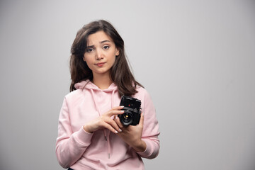 Female photographer with camera standing on gray background