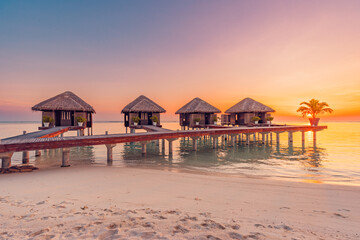 Sunset in Maldives island. Beautiful sunset sky and clouds, luxury water villas and wooden pier pathway. Exotic summer travel destination, vacation background, inspirational sea horizon. Tropical sun