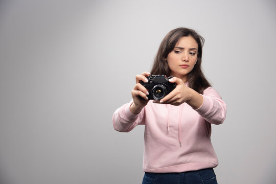 Pretty young woman taking pictures with camera over a gray wall