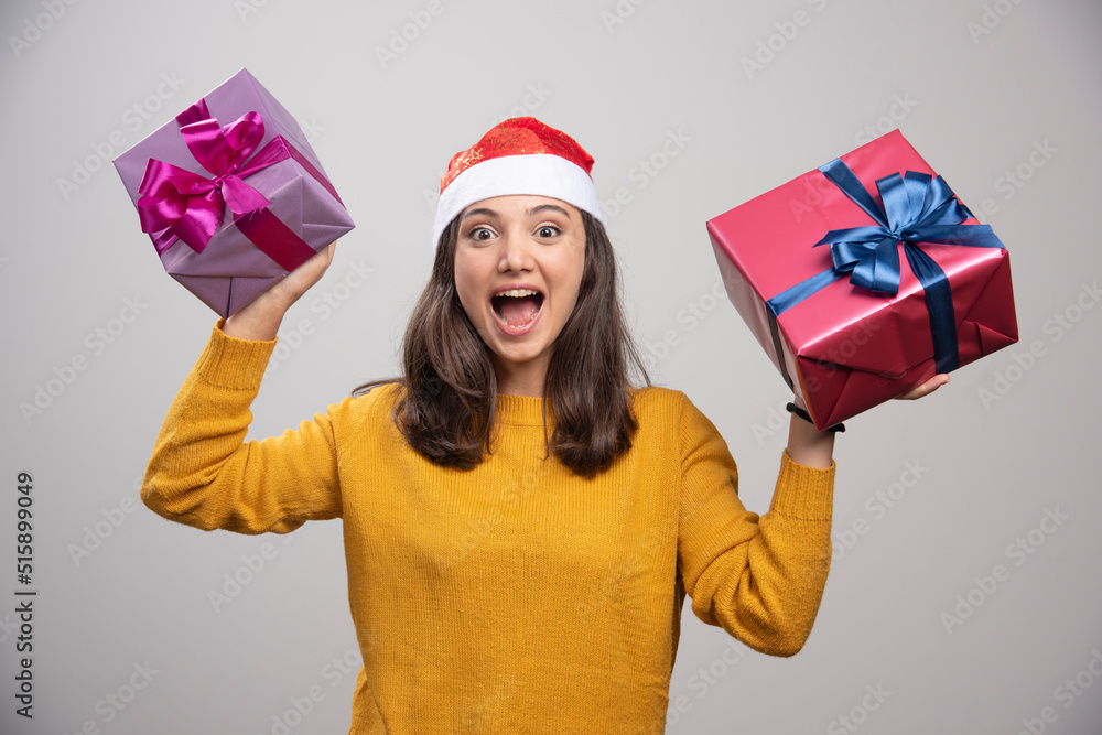 Wall mural Young woman in Santa hat holding gift boxes and feeling happy