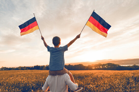 Patriotic father and child waving Germany flag on sunset