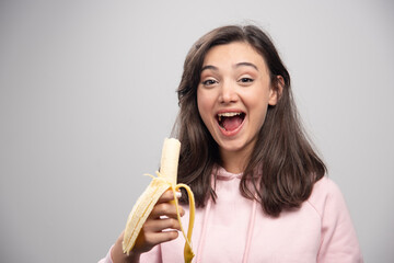 Young woman eating banana over gray background