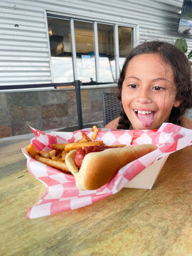 young girl sitting and staring hungrily at fresh hot dog and fries with tongue out delicious meal outdoor summer fun