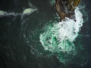 Shooting from the air. Turquoise water of the ocean, white foamy waves crashing against the rocky shore. Abstraction. The beauty and majesty of nature. Environmental Protection.