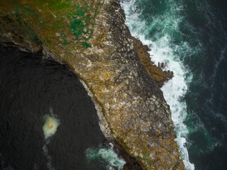 View from above. An island overgrown with green grass and moss in the ocean. white waves crash on the shore. Desert place. Travel, tourism, recreation, relaxation, fresh sea air.