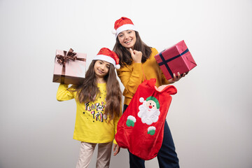 Two young girls with Christmas presents standing over a white wall