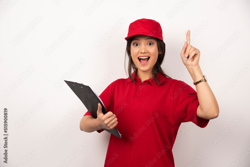 Wall mural Young delivery woman in red uniform with clipboard on white background