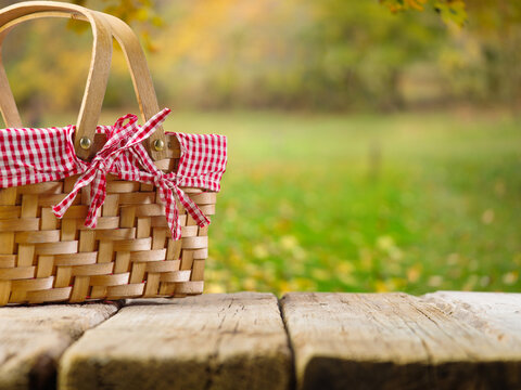On a simple wooden table, a straw, beautifully decorated picnic basket against the backdrop of picturesque autumn nature. Recreation, picnic, harvest day celebration, thanksgiving day.
