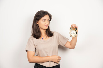 Young woman looking alarm clock angrily