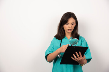 Female doctor looking at results with magnifying glass on white background