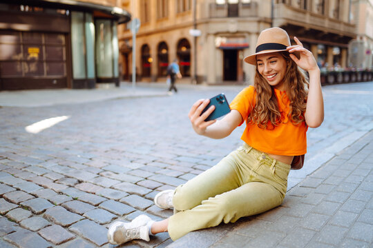 Selfie time. Young woman olding mobile phone taking selfie photo using smartphone camera. Beautiful girl walks through the streets  and takes pictures of some sights .Lifestyle, travel, tourism.