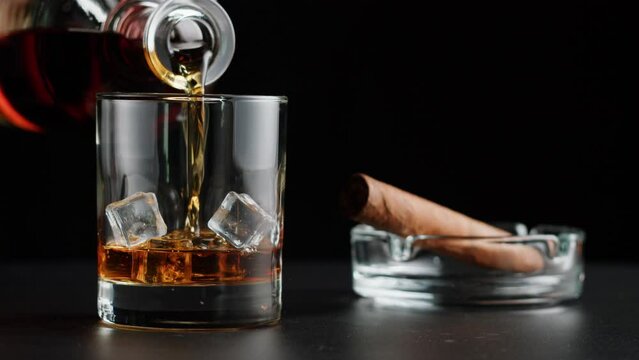 Brandy or whiskey and cigar close-up. Luxury cognac with ice on black background. Alcohol amber drink, drinking rum, liqour beverage in glass.
