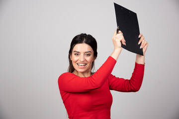 A happy woman with pen and clipboard on a gray background.
