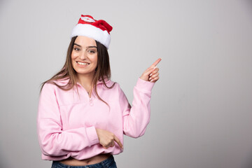 Portrait of joyful woman in red Santa's Claus hat pointing up to the side