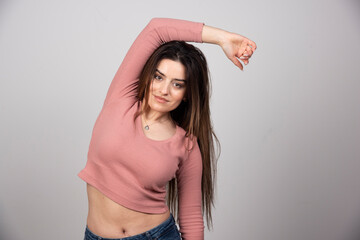 Pretty smiling woman posing in studio with hands overhead near the gray wall