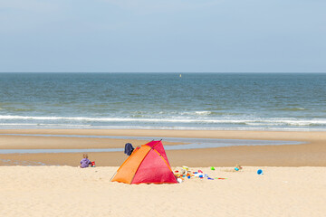 A child sitting by the seashore playing next to a tent and a bunch of toys