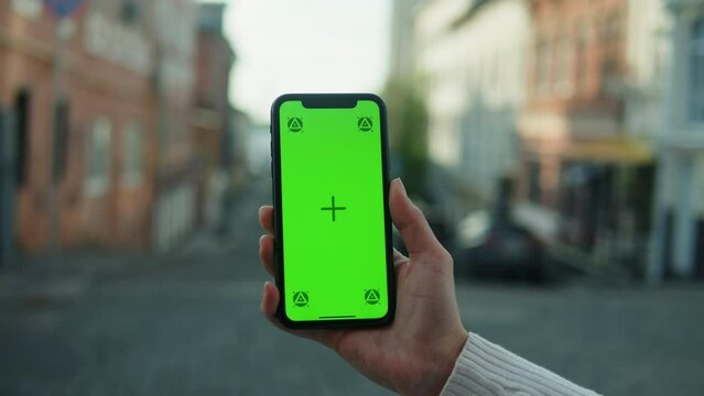 Woman holding smartphone with chroma key close-up. Young female person using phone with green screen outdoor.