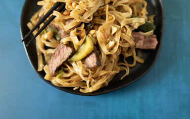 An asian noodle bowl with thinly sliced steak, rice noodles and vegetables