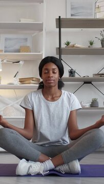 Vertical video. Home meditation. Calm woman. Yoga practice. Peaceful lady in sportswear sitting lotus pose on fitness mat light room interior.