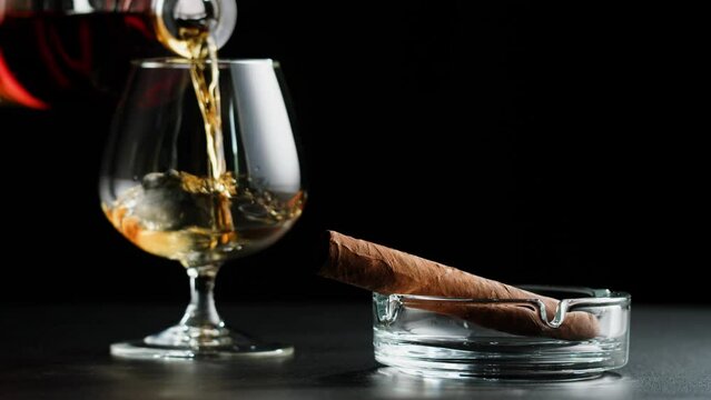 Brandy or whiskey and cigar close-up. Luxury cognac on black background. Alcohol amber drink, drinking rum, liqour beverage in glass.