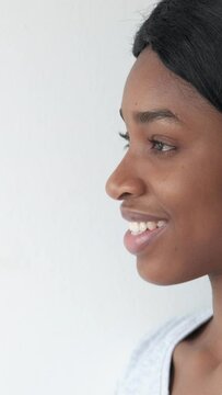 Vertical video. Profile portrait. Female model. Positive mood. Optimistic side view face of pretty smiling black woman on white background.