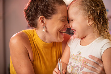 Imagem de m&atilde;e e filha brincando enquanto cozinham um bolo. Mulher loira brincando com sua filha na cozinha. Receita de doce feita em fam&iacute;lia.