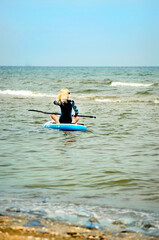 A blond woman in a wetsuit, engaged in snorkeling, sits on a board with an oar.