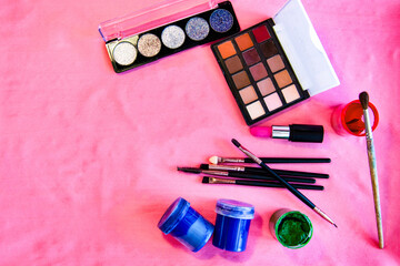 Decorative cosmetics (eyeshadow, lipstick) on a pink background, along with paints and brushes for...