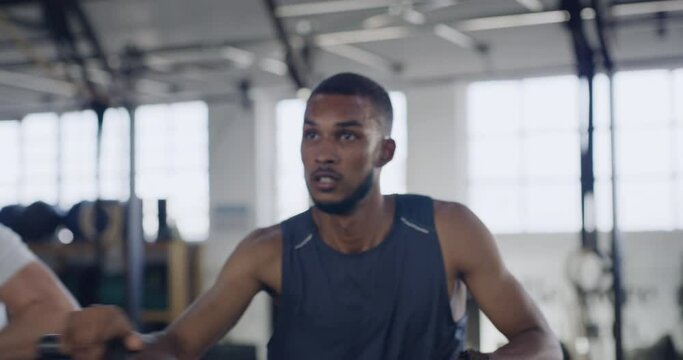 Serious and sporty people during a spinning class at the gym. Fit people using air bikes for cardio exercise in a fitness facility. Group of sweaty men and women listening to music while exercising
