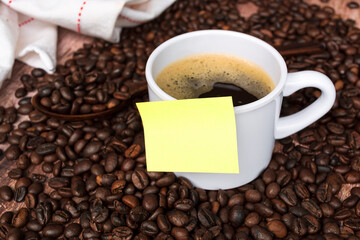 Yellow sticky note on a cup of coffee and coffee beans background.