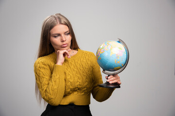 Blonde girl holding a globe and checking world map