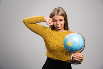 Blonde girl holding a globe and looking tired and sleepy