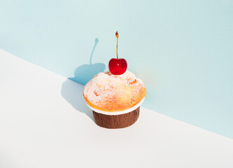 Cupcake with cherry against pastel blue and white background. Sunny day shadow. Minimal food concept.
