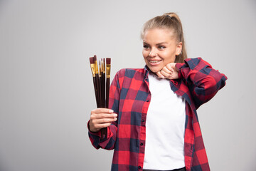 Blonde artist in checked shirt feels positive and happy with paint brushes in the hand
