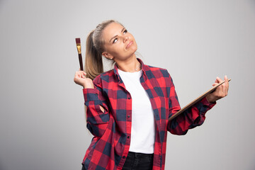 Blonde artist in checked shirt feels glamour and confident with paint brushes in the hand