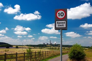 UK road sign 10 mph speed limit. The country road leads to a power station. Blue cloudy sky.