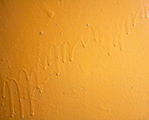 Old paint streaks. Dried orange-yellow dry paint on the wall artistic background.Drops of paint on the wall.