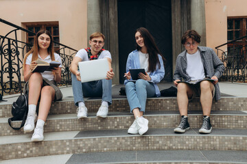 Fototapeta premium Confident students. Group of happy young people working together and looking at laptop while sitting on steps