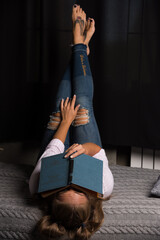 Woman lying on bed and put book on her face on dark background