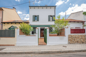 Single-family urban residential building facades painted white with green windows and shutters, sun awning, plants and metal door