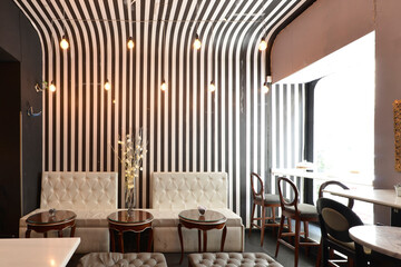 Room of a cafeteria with charming wooden furniture and sofas and stools upholstered in white capitone